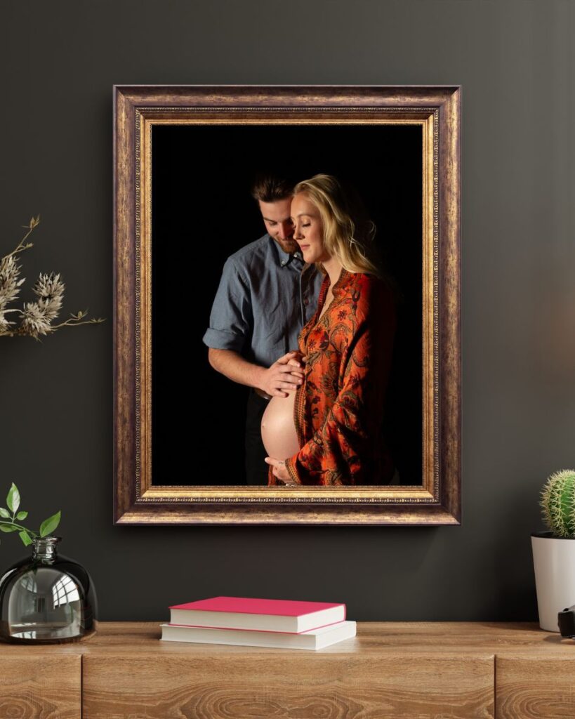 wall art mockup of a pregnancy portrait on dark background of a young Rock Hill SC couple framed in gold. Appears to be a common space. Mom to be is wearing her heirloom scarf from her grandmother's collection to signify to continued family line.