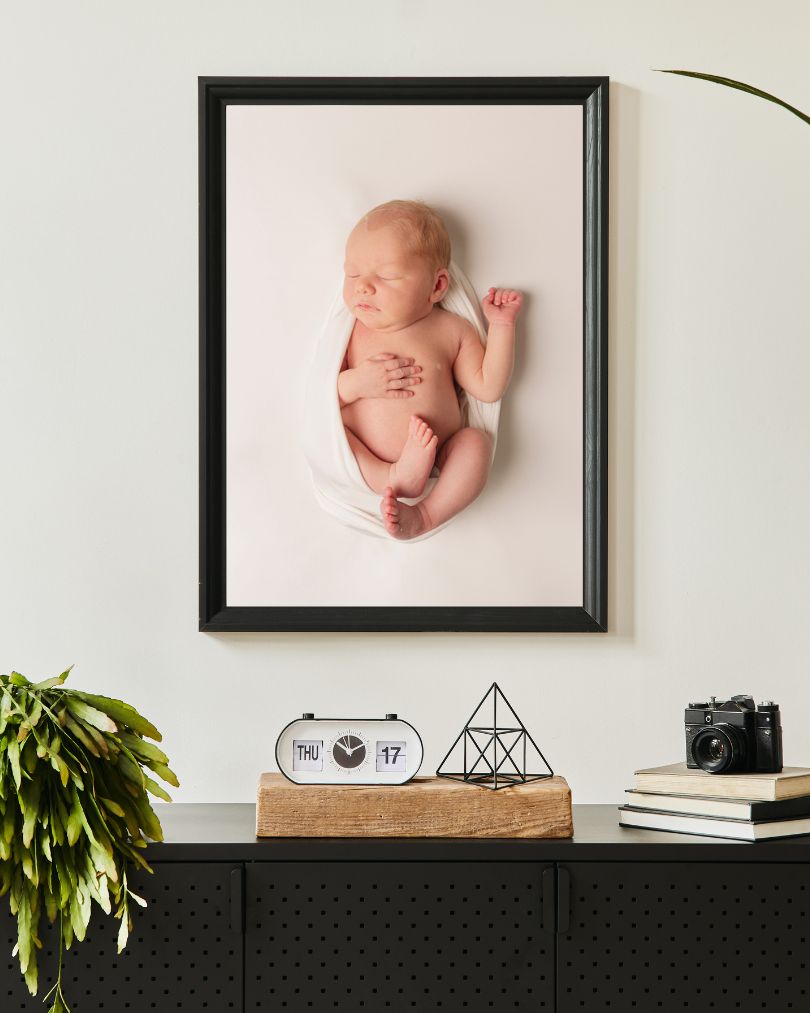 Adorable newborn baby wrapped in white, seen in a portrait displayed in a mock up entry way, along with this article on how to prepare your home for baby, by Charlotte newborn photographer