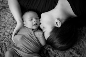 mom kissing baby boy swaddled one month old, black and white image