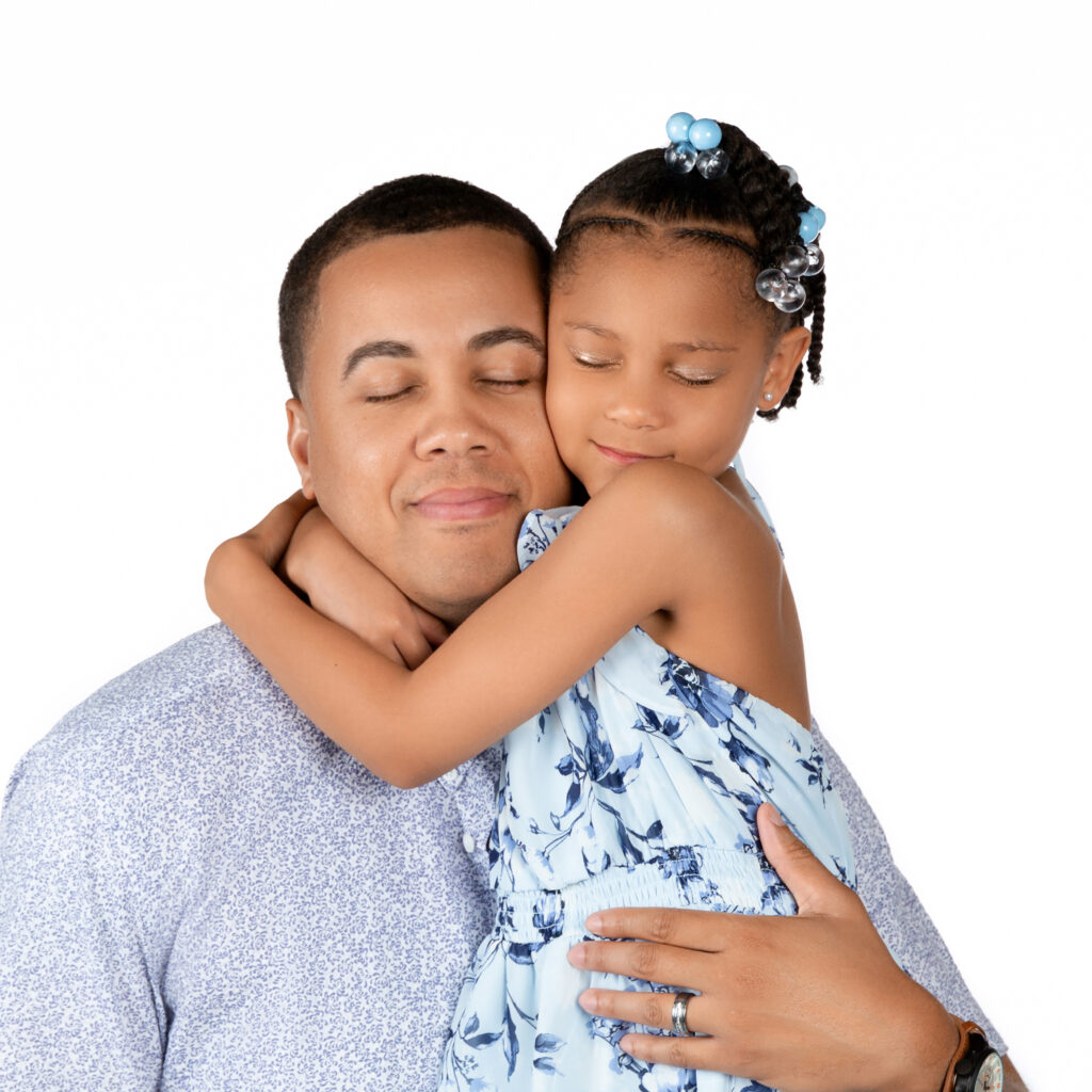 portrait of dad and daughter hugging with closed eyes wearing light blue.