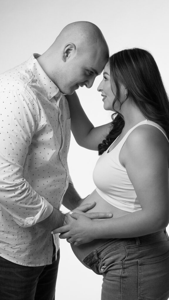 black and white pregnancy portrait, charlotte nc parents tobe gazing lovingly into each others eyes, while they both caress mom's pregnant belly, dressed casually in jeans and simple white tops. 