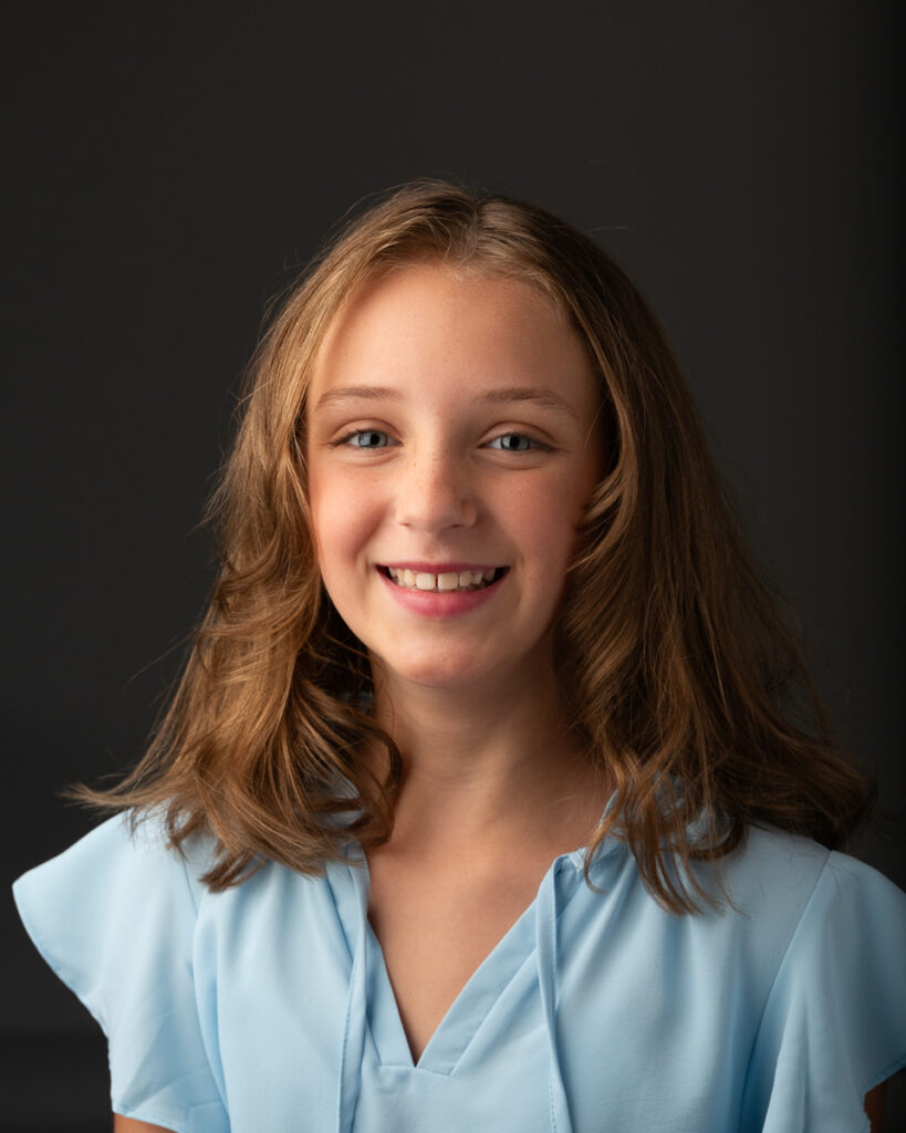 Young white lady smiling at camera with traditional Charlotte Headshot setup on dark background for her modeling comp card